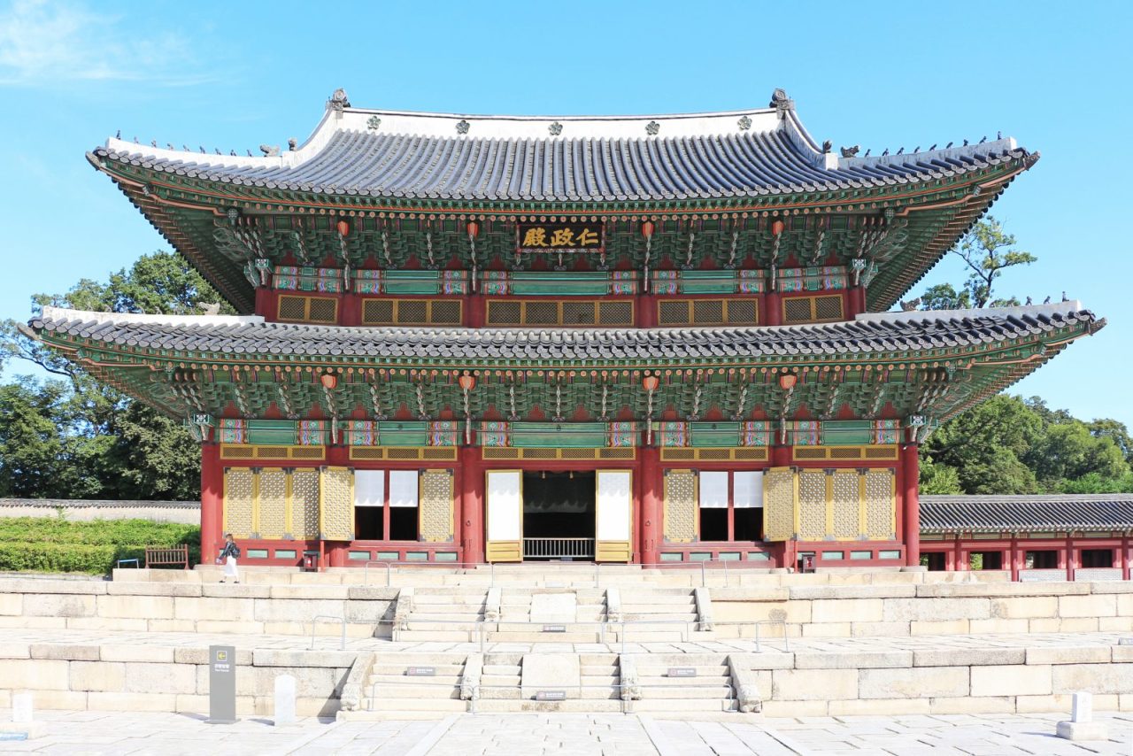 Injeongjeon Hall at Changdeokgung Palace in Seoul, with ornate painted eaves above a stone terrace under a blue sky.